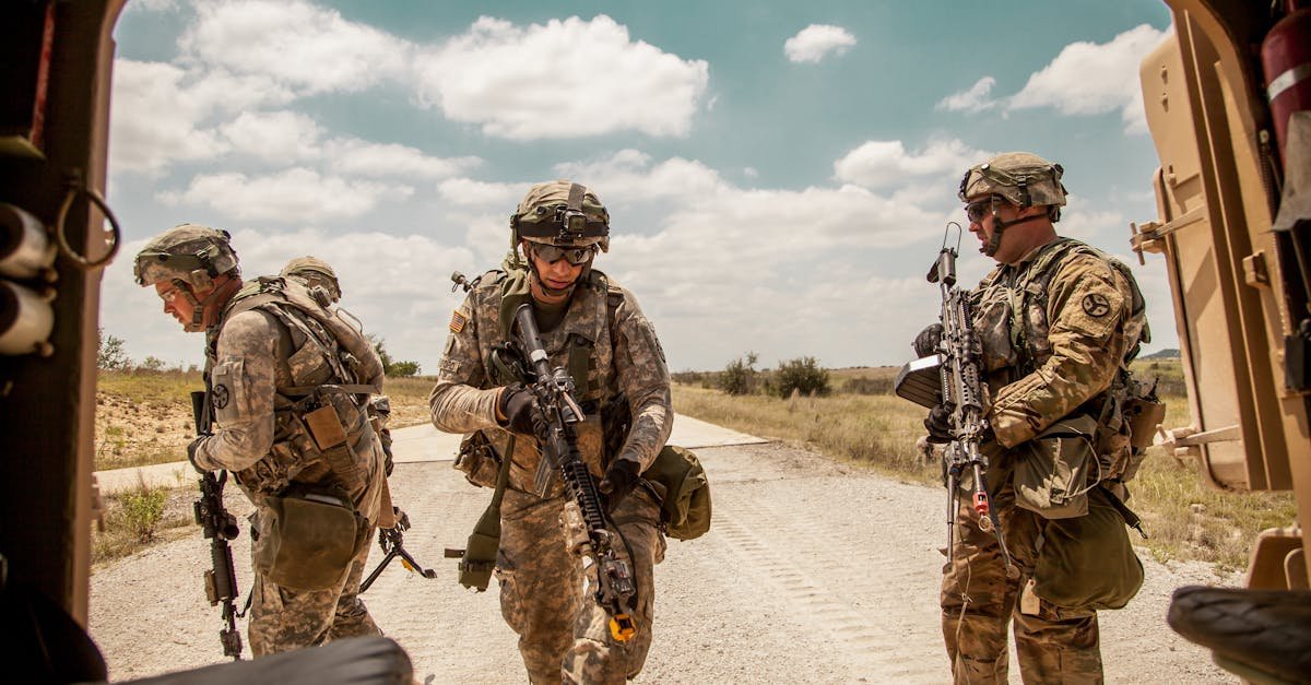Three soldiers in camouflage gear with rifles in an outdoor military training exercise.